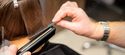 Close up of the hairdresser straightening the short hair of a female client with a hair straightening iron in a beauty salon