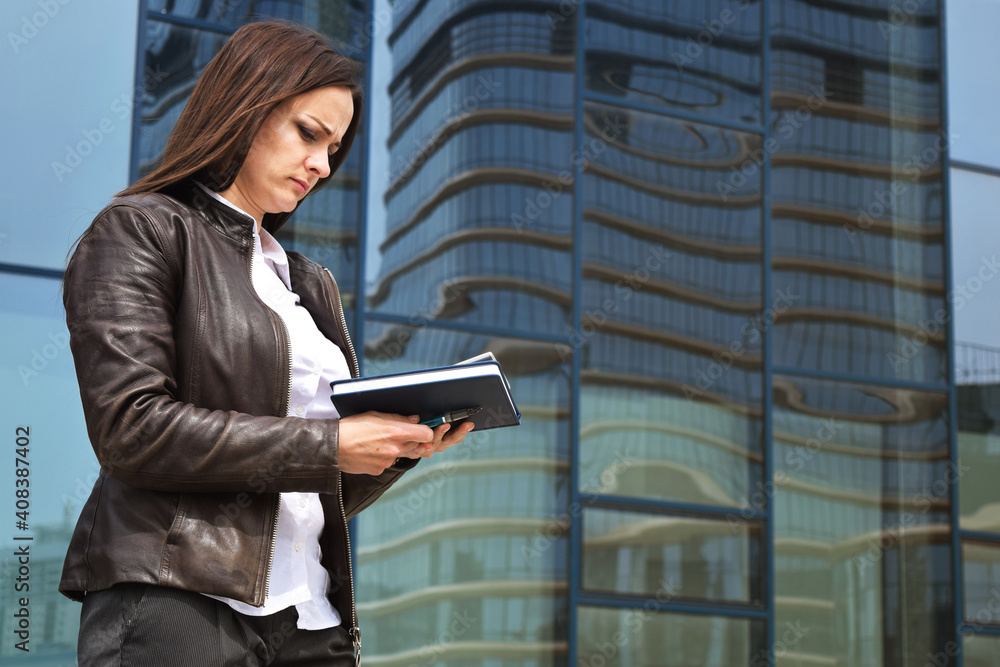 Young business woman checks mail on her mobile phone on a city street. Stylish fashion model in a business suit. Young business woman checks mail on her mobile phone on a city street. Stylish fashion model in a business suit.