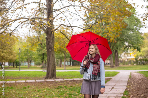 Young woman with umbrella walking in park during autumn photo