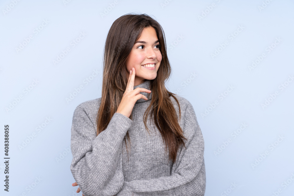 Teenager Brazilian girl over isolated blue background thinking an idea while looking up Teenager Brazilian girl over isolated blue background thinking an idea while looking up