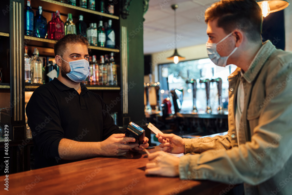 Male customer paying with credit card to waiter in bar during pandemic Male customer paying with credit card to waiter in bar during pandemic