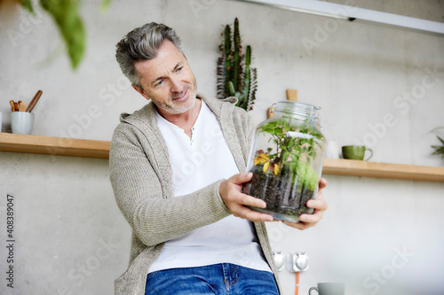 Smiling man holding terrarium while sitting at home photo