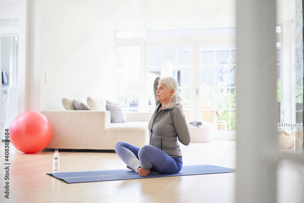 Senior woman exercising with hands behind back in living room Senior woman exercising with hands behind back in living room