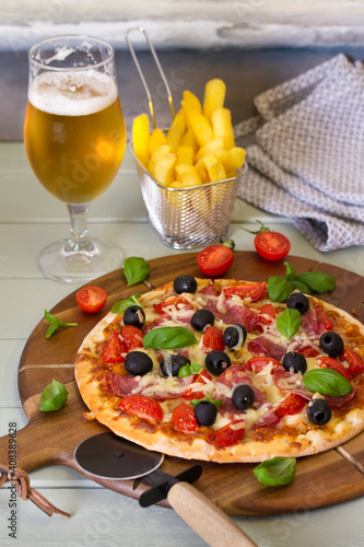 Delicious pizza served on wooden pizza board. Glass of beer and french fries