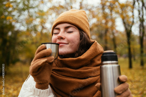 Young woman with eyes closed smelling tea in autumn park photo