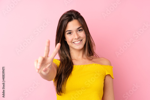 Teenager Brazilian girl over isolated pink background smiling and showing victory sign
