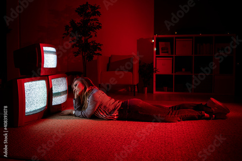 Young woman with hand in hair lying on floor in front of old TV's at living room photo