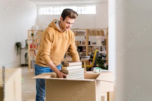 Young man packing books in cardboard box in new loft apartment photo