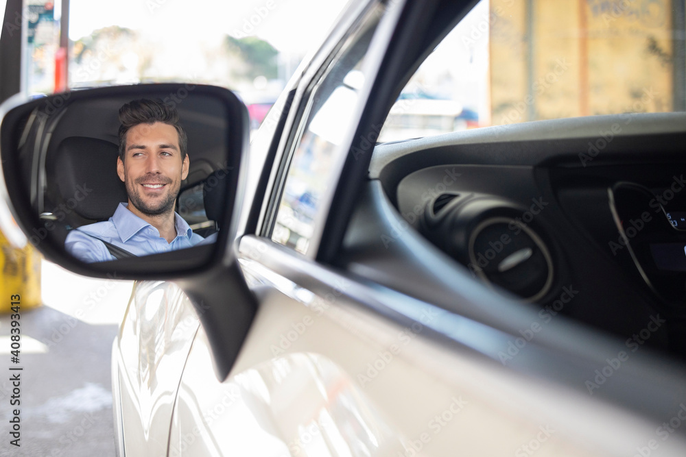 Wing mirror reflection of businessman smiling while driving car
