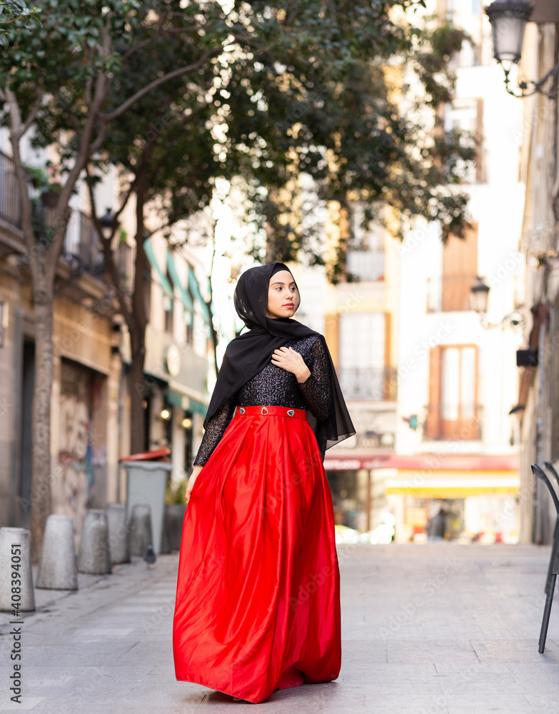 Portrait of young woman wearing hijab and long skirt walking along sidewalk Portrait of young woman wearing hijab and long skirt walking along sidewalk