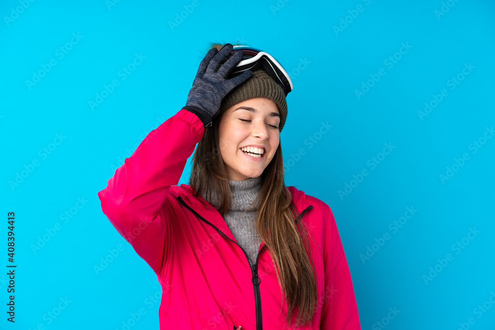 Teenager skier girl with snowboarding glasses over isolated blue background laughing Teenager skier girl with snowboarding glasses over isolated blue background laughing