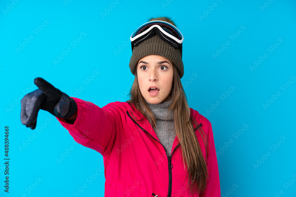 Teenager skier girl with snowboarding glasses over isolated blue background pointing away Teenager skier girl with snowboarding glasses over isolated blue background pointing away