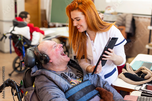 Smiling nurse showing digital tablet to happy disabled man in nursing home
