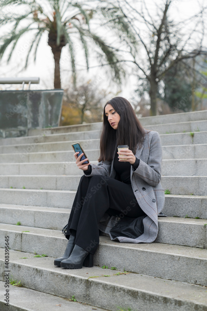 Fashionable businesswoman using mobile phone while having coffee on staircase Fashionable businesswoman using mobile phone while having coffee on staircase