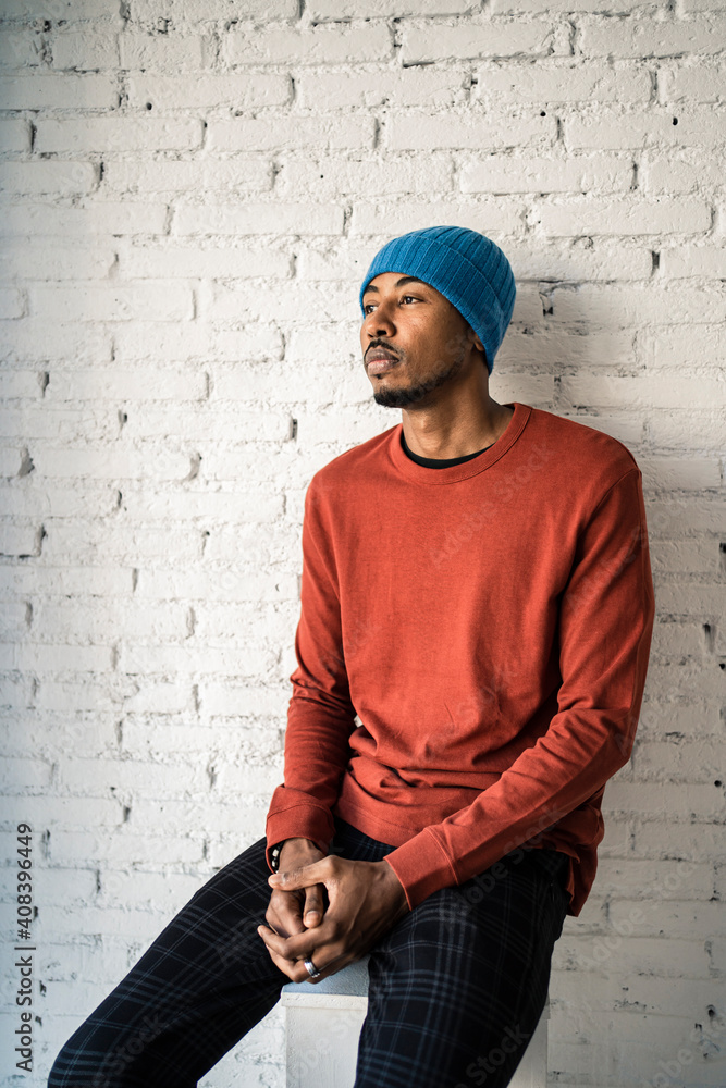 Thoughtful man looking away while sitting on pedestal against white brick wall Thoughtful man looking away while sitting on pedestal against white brick wall