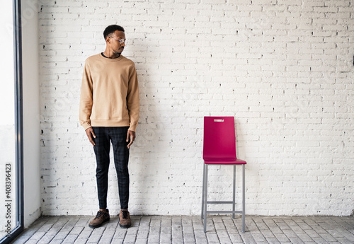 Mid adult man wearing eyeglasses standing by chair against white brick wall photo