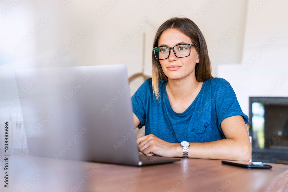 Businesswoman wearing eyeglasses looking at laptop in home office Businesswoman wearing eyeglasses looking at laptop in home office
