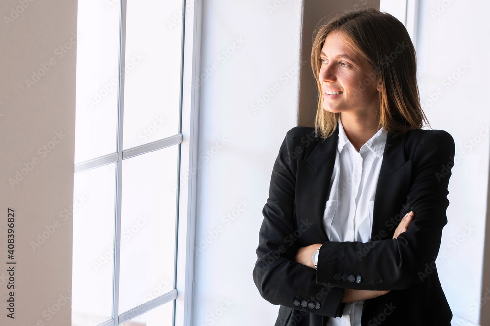 Thoughtful young businesswoman with arms crossed while looking through window at home Thoughtful young businesswoman with arms crossed while looking through window at home
