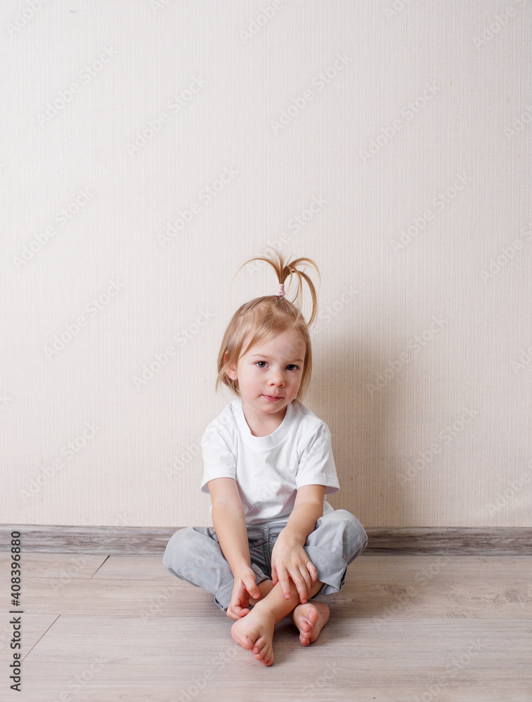 little girl B is sitting on the floor of the room against the wall. little girl B is sitting on the floor of the room against the wall.