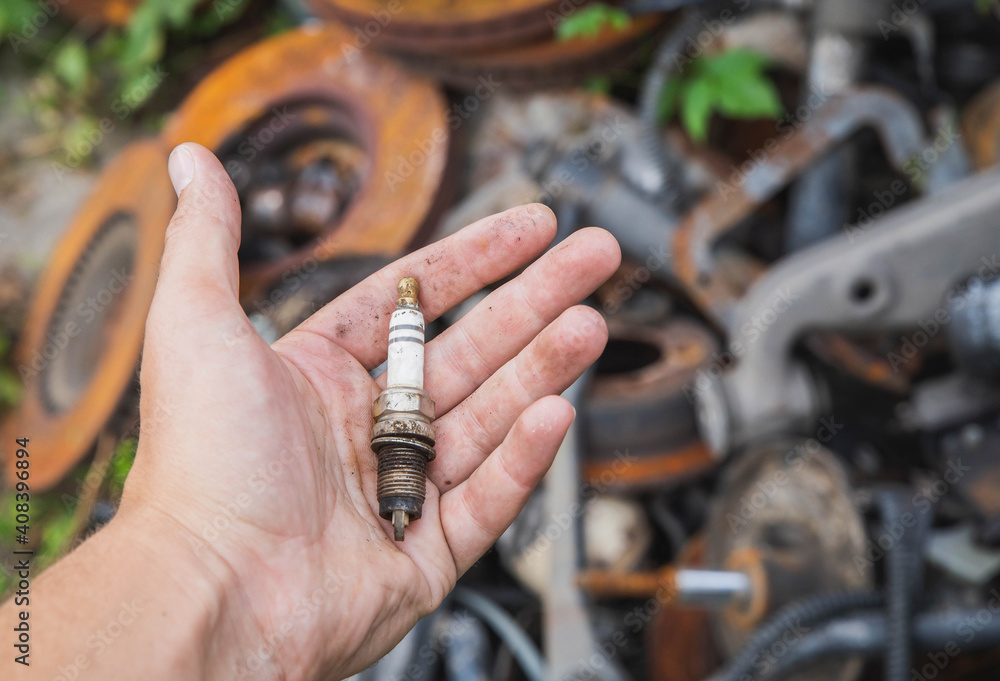 Stockfoto old spark plug in hand near a pile of rusty spare parts in a