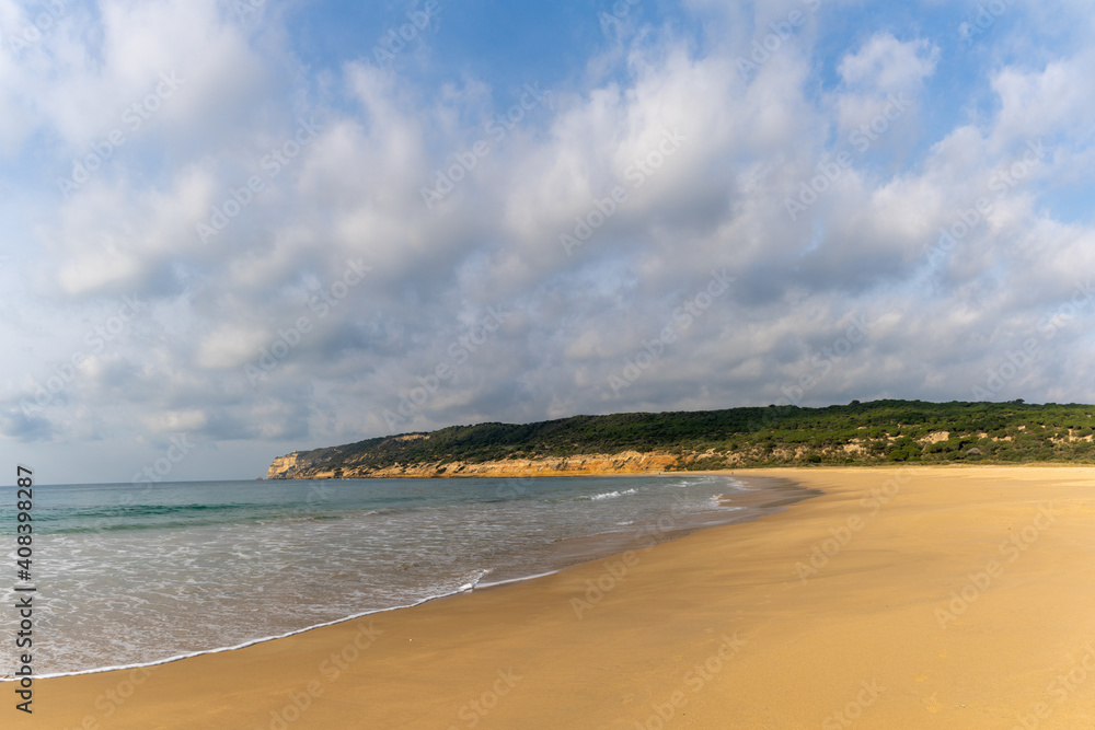 peaceful sandy beach with gentle waves and tree covered cliffs in the background