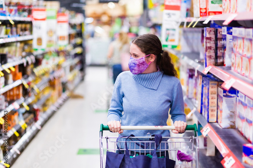 Young woman in her twenties wearing a face mask in shopping aisle, choosing what to buy