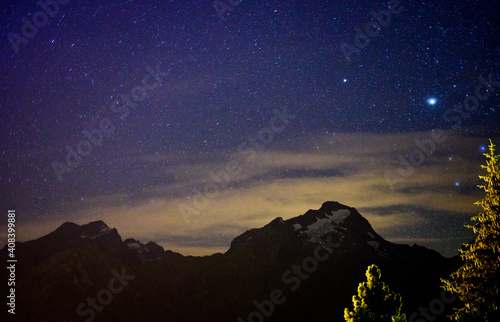 Evergreen fir tree with cones, peaks of French Alps mountains and starry sky at night on background photo