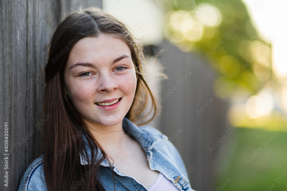 Portrait of happy teenage girl leaning on wooden backyard fence after school Portrait of happy teenage girl leaning on wooden backyard fence after school