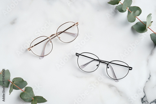 Women's glasses and eucalyptus leaves on marble table top view photo