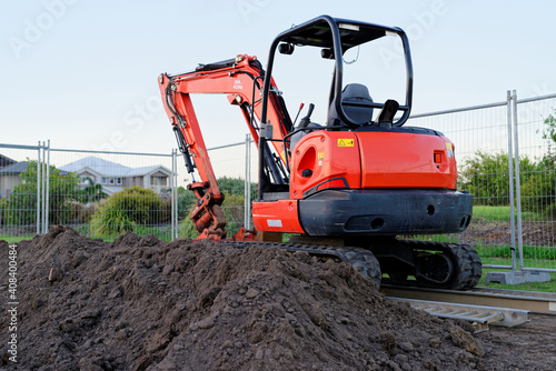 Mini digger standing idle at a construction site - red excavator photo