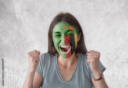 Young woman with painted flag of Zambia and open mouth looking energetic with fists up