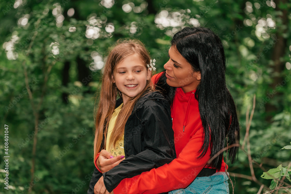 Fototapeta premium Beautiful mother and her cute daughter sitting in forest and talking, spending good time in spring nature