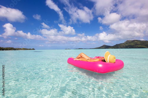 Woman relaxes on pink inflatable mattress over clear turquoise ocean water near a tropical island