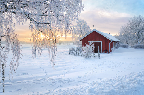 Winter view of a red barn at sunset in Rusko, Finland. Trees covered with snow.