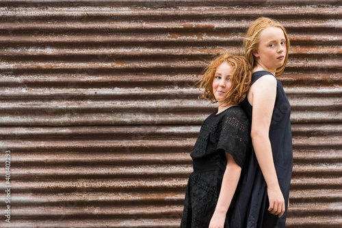 two red headed girls in black dresses back to back against rusty brown corrugated iron shed photo