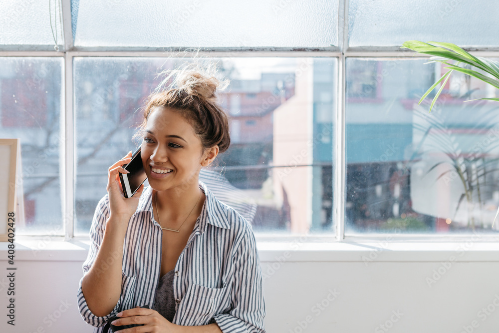 Young female talking on a mobile phone in a bright studio office Young female talking on a mobile phone in a bright studio office
