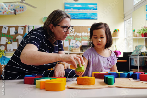 Multicultural teacher and child playing wooden blocks puzzles in kindergarten