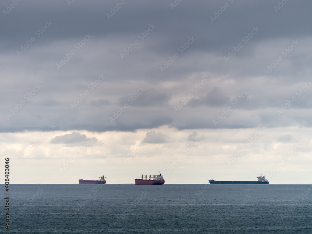 Three bulk carriers on the horizon on a cloudy day Three bulk carriers on the horizon on a cloudy day