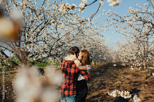 Young romantic couple in love is hugging among apple trees in blossom in spring sunny warm day. © eduard