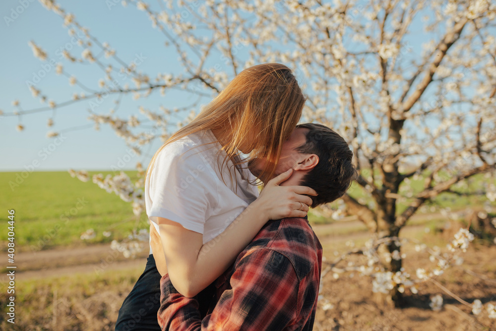 Loving couple kissing and hugging near blossoming tree in spring day. 