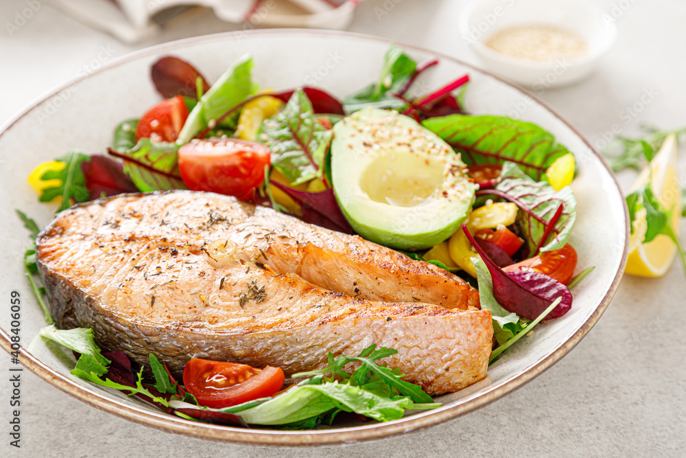 Salmon fish steak grilled, avocado and fresh vegetable salad with tomato, bell pepper and leafy vegetables