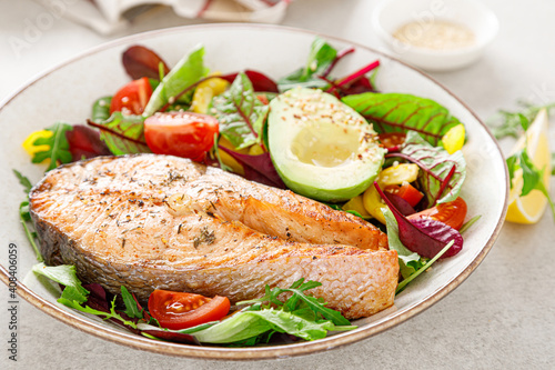 Salmon fish steak grilled, avocado and fresh vegetable salad with tomato, bell pepper and leafy vegetables