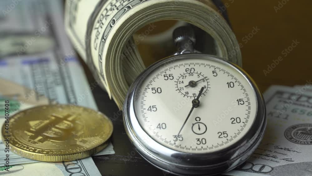Bitcoin BTC with stopwatch lies on dollars bills. Time is money concept. Currency or cash revenue. Cryptocurrency or trade concept. Record high boosted by increased demand from retail investors Bitcoin BTC with stopwatch lies on dollars bills. Time is money concept. Currency or cash revenue. Cryptocurrency or trade concept. Record high boosted by increased demand from retail investors