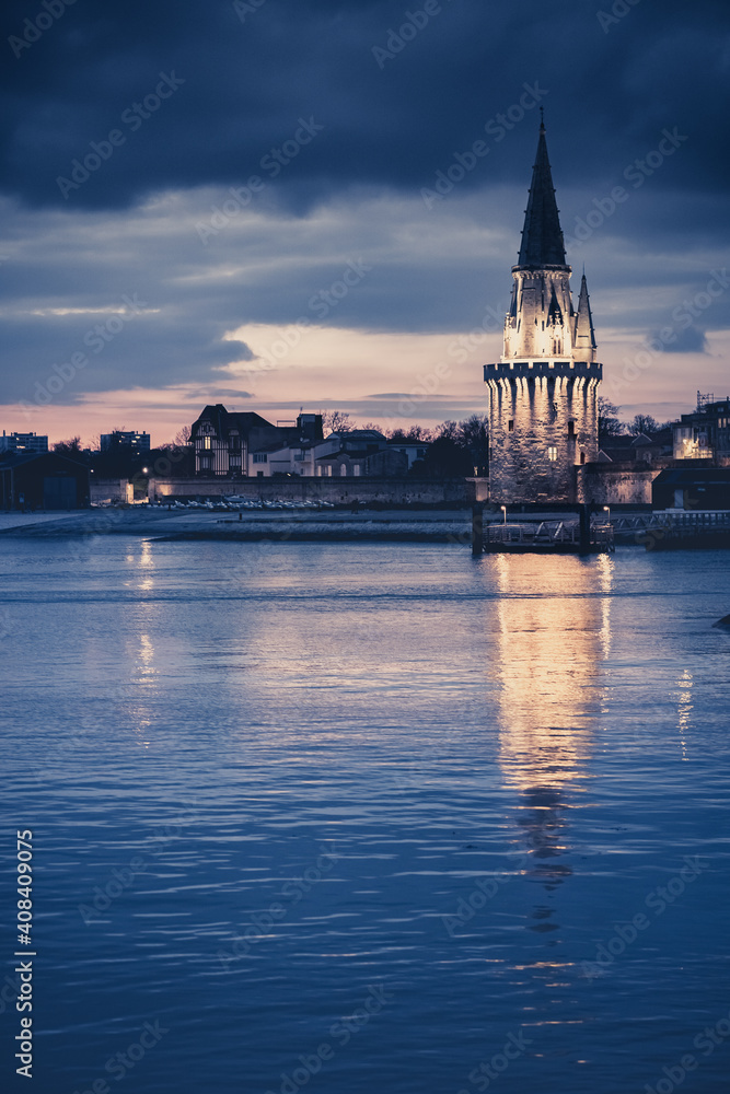 Obraz premium Night view of the Tour de la lanterne in La Rochelle, France. beautiful reflections in the harbor water.