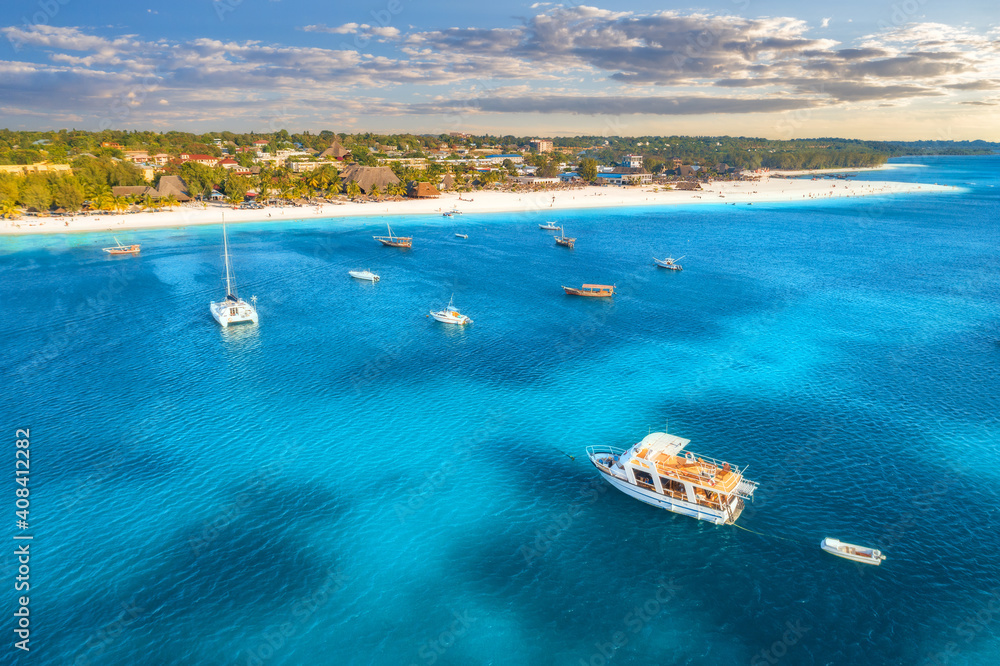 Aerial view of the yachts and boats on tropical sea coast with sandy beach at sunset. Summer holiday in Zanzibar, Africa. Landscape with boat, yacht, clear blue water, green palm trees, sky. Top view Aerial view of the yachts and boats on tropical sea coast with sandy beach at sunset. Summer holiday in Zanzibar, Africa. Landscape with boat, yacht, clear blue water, green palm trees, sky. Top view