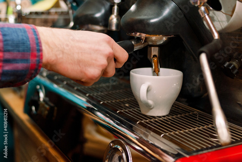 Male hands of the barista near the coffee machine. Barista makes cappuccino with a coffee machine. The coffee from the machine is poured into a classic white cup. Popular hot drinks. Men's work. 
