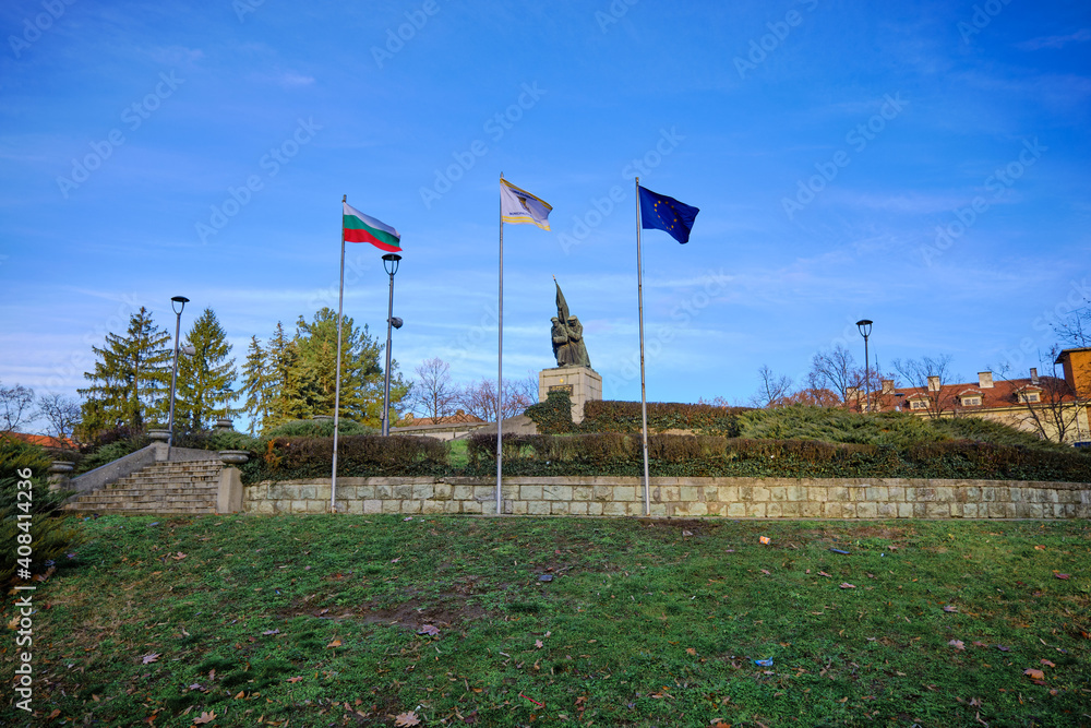 Liberators Monument in Kardzhali, Bulgaria in a Park with EU, Bulgaria flags. Statue on green grass, blue sky and mountain background. Liberators Monument in Kardzhali, Bulgaria in a Park with EU, Bulgaria flags. Statue on green grass, blue sky and mountain background.