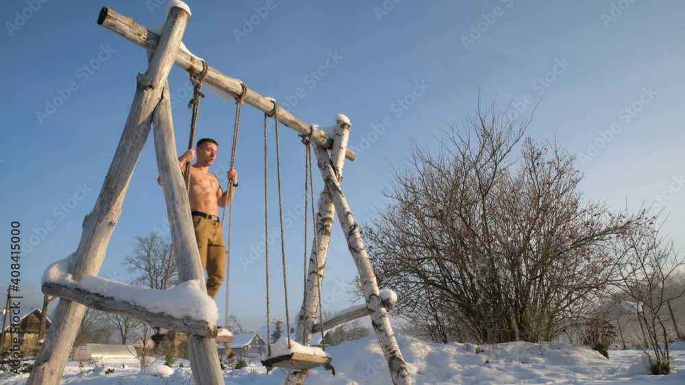Man swinging on a rope swing in a snowy winter Man swinging on a rope swing in a snowy winter