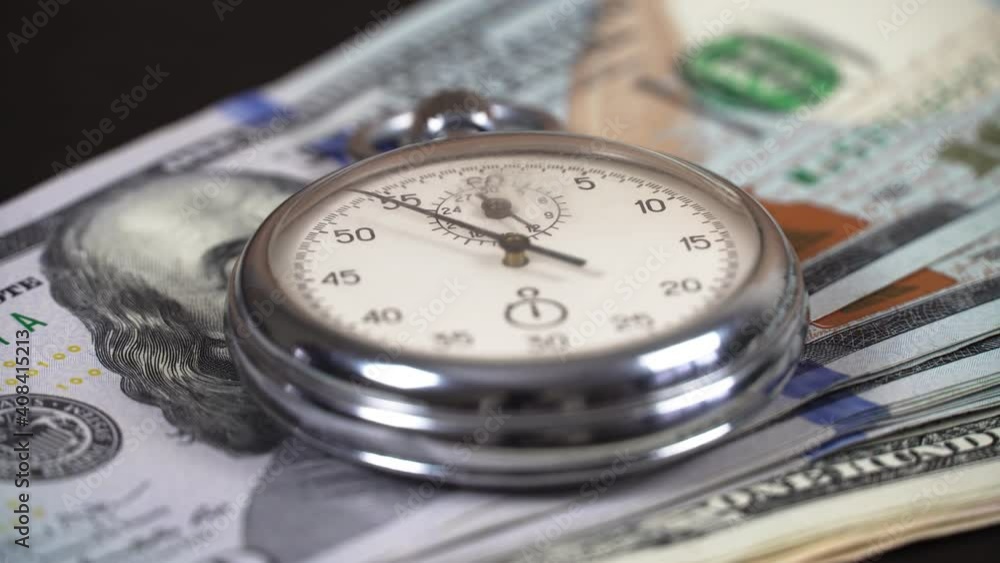 The stopwatch is on top of the 100 dollars bills and the hand is ticking. The concept of sales, discounts and investments in stocks and businesses. The stopwatch is on top of the 100 dollars bills and the hand is ticking. The concept of sales, discounts and investments in stocks and businesses.