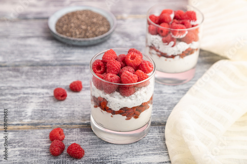 Yogurt with raspberry, goji berries and chia seeds in glass on gray wooden background. Side view, selective focus.